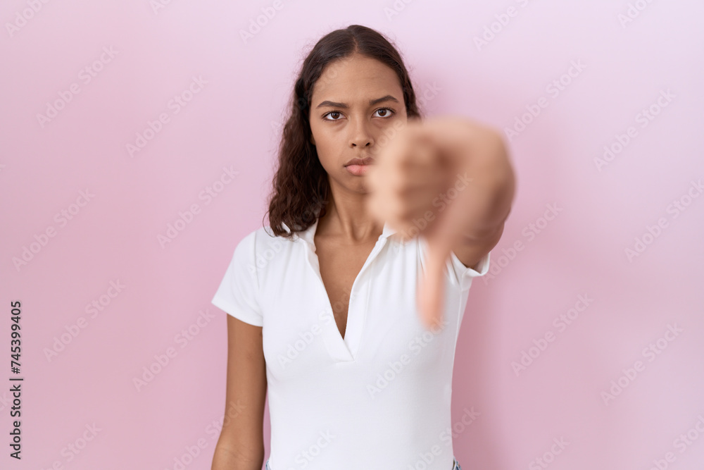 Poster young hispanic woman wearing casual white t shirt looking unhappy and angry showing rejection and ne