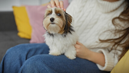 Hispanic woman caresses her biewer terrier inside a cozy living room, showcasing companionship and...