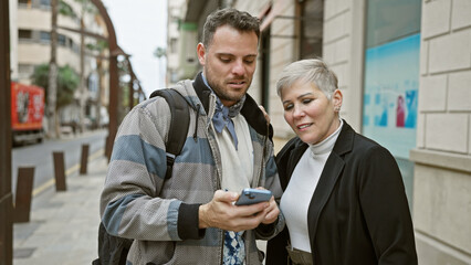 A man and woman check a smartphone together on a city street, embodying urban connection and navigation.