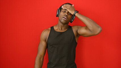 Young african american man with headphones against a red wall looking stressed.