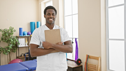 Portrait of a confident young african american man, a healthcare professional, standing in a bright rehabilitation clinic.