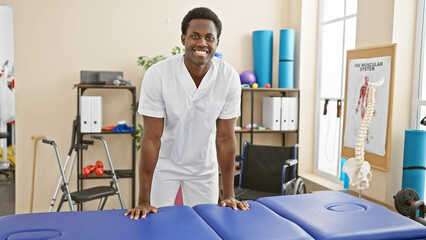 Smiling african american male therapist in a rehab clinic room with medical equipment