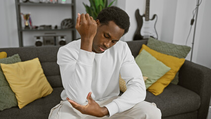 A young man experiencing elbow pain in a modern living room setting, wearing casual attire.