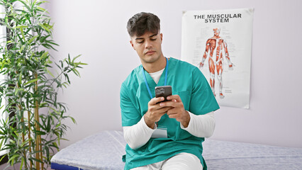 Young, handsome hispanic man physiotherapist sporting a serious face while using a smartphone in a bustling rehab clinic