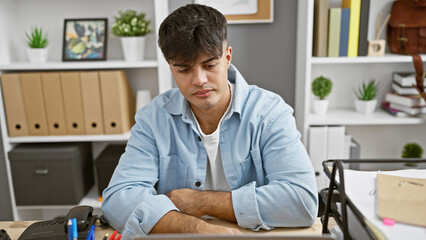 Focused young hispanic man working hard, serious business worker sitting with arms crossed gesture at office desk, portrait of a successful professional boss