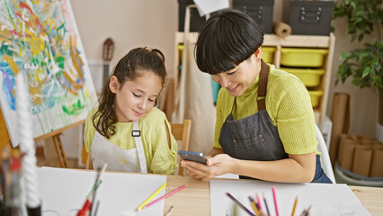 Teacher and student, two painters at heart, bonding over art lesson in studio, joyfully drawing and texting in notebook using smartphone