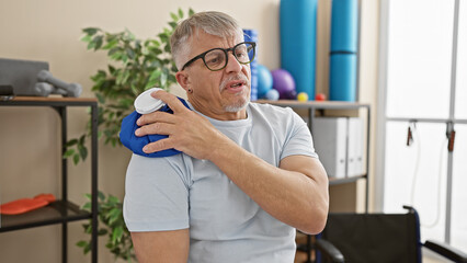Mature man in clinics rehabilitation room using ice pack on shoulder