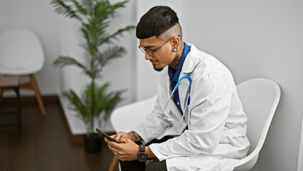 Handsome young latin doctor visibly serious, tirelessly working, texting on a smartphone in the...