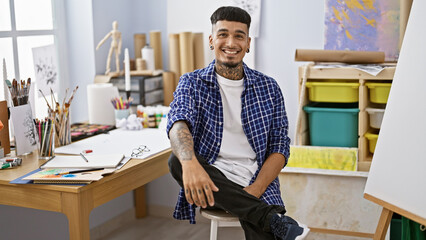 Smiling young latin artist, oozing confidence, enjoys his craft in the cozy corner of an art...
