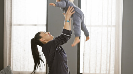 A joyful mother lifts her toddler in a bright bedroom, depicting love and family bonding indoors.