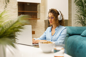 Positive woman in headphones typing on laptop while in living room