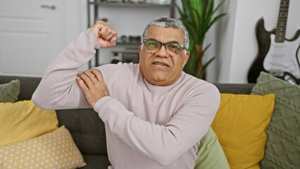 A mature man with glasses showing muscle in a cozy living room
