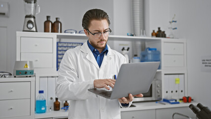 Young hispanic man scientist using laptop at laboratory