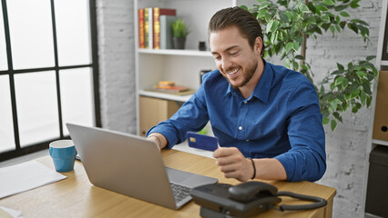 Obraz premium Young hispanic man business worker shopping with laptop and credit card smiling at the office