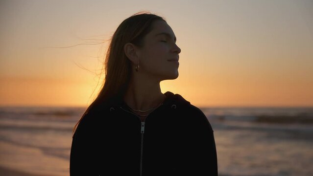 Casually dressed young woman with eyes closed enjoying peace and beauty of beautiful sunrise morning over beach and sea in South Africa - shot in slow motion