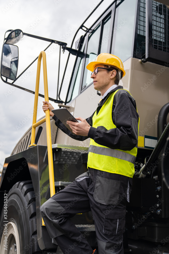 Poster Engineer with tablet computer stands on the stairs to the cab of a truck..