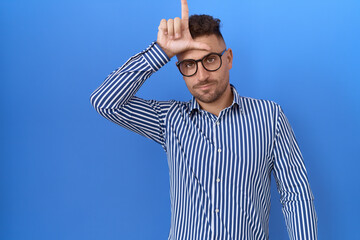 Hispanic man with beard wearing glasses making fun of people with fingers on forehead doing loser...