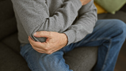 A middle-aged man with grey hair experiencing elbow pain at home, conveying a sense of discomfort.
