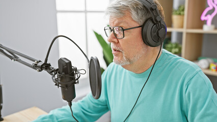 Mature man with headphones speaks into a microphone in a radio studio, portraying a professional...