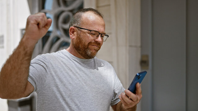 Eureka! cheerful middle-aged caucasian man with beard, firstly celebrating using smartphone on outdoor city street, texting a winning message!