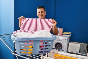 Young latin man smiling confident hanging clothes on clothesline at laundry room