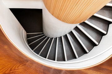 Black spiral staircase goes down in wooden interior, top view