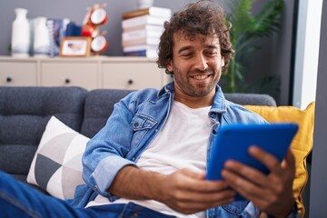 Young hispanic man using touchpad sitting on sofa at home