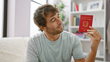 Young man smiling holding passport of italy sitting on the sofa at home