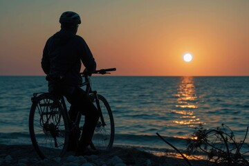 Man by bicycle on beach at sunset, wheel touching water, under sky