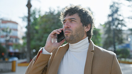 A focused hispanic man with a beard talking on a smartphone in a sunny urban park