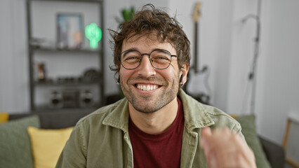 Happy young hispanic man with glasses and beard smiling indoors, wearing casual clothes and...