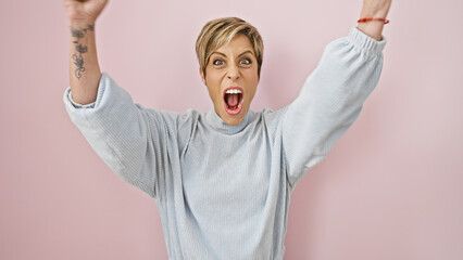 Excited woman with short blonde hair celebrating against a pink wall, portraying youthful energy...