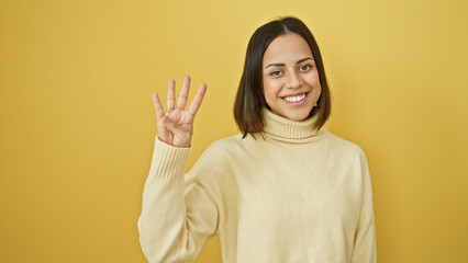 Fototapeta premium Smiling young hispanic woman posing against a yellow isolated background, cheerfully gesturing four with her hand