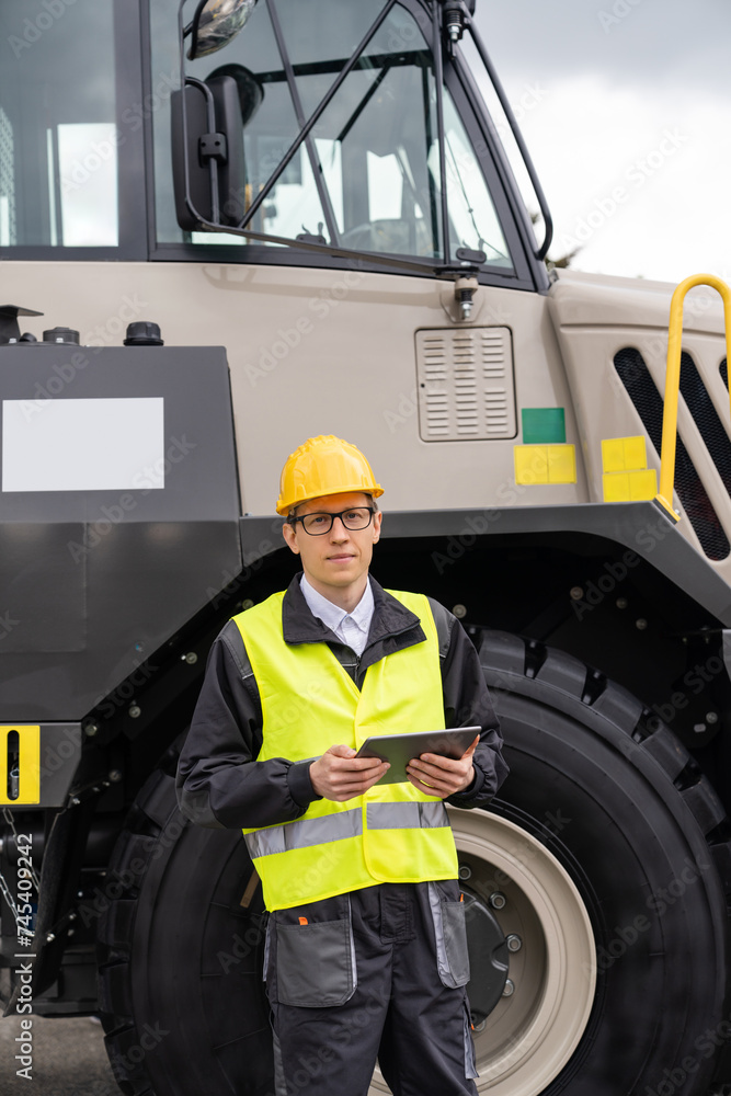 Poster Man worker with tablet computer stands next to mining truck