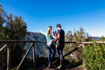 Hiker family with baby standing at wooden railing overlooking lush green mountains and hills seen...