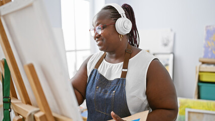 Confident african american woman artist drawing with passion, listening to music in art studio, embracing her curves and smiling