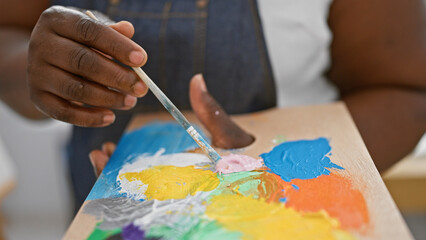 Creative hands of an african american woman artist passionately mixing color on palette in a...