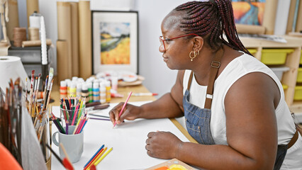 Focused african american woman, captivating artist, drawing with concentration on her notebook at...