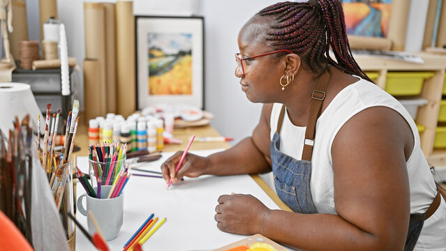Focused african american woman, captivating artist, drawing with concentration on her notebook at an indoor art studio.