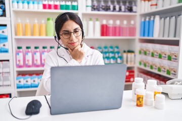 Young arab woman working at pharmacy drugstore using laptop looking confident at the camera with...