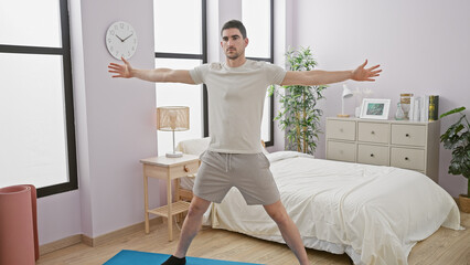 Handsome young man stretching arms in spacious bedroom interior