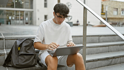 Cool hispanic teenager, a smart university student, sits on urban campus stairs, deeply engrossed in online study on his laptop. looking serious yet relaxed, living the casual city lifestyle. - Powered by Adobe