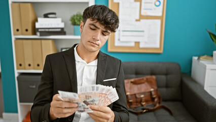 Handsome young hispanic teenager making business banknotes count â€“ working a serious, focused job indoors, surrounded by icelandic krona in a relaxed office.