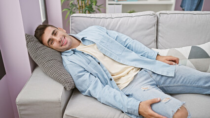 Happy male portrait, confident, handsome young hispanic man relaxing, resting on the cozy sofa indoors. enjoying, reveling in the comfort of home, with a joyful smile lighting up his face.