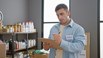 Dedicated young hispanic man volunteering at charity center, meticulously writing on checklist...
