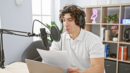 Hispanic man with curly hair wearing headphones speaks into a microphone in a radio studio.