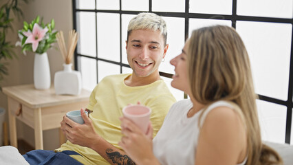 Beautiful couple drinking cup of coffee sitting on bed at bedroom