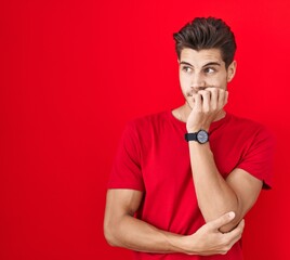 Young hispanic man standing over red background looking stressed and nervous with hands on mouth biting nails. anxiety problem.