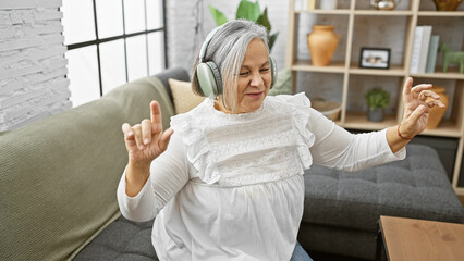 A joyous elderly woman enjoying music with headphones in a cozy living room