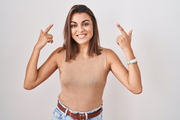 Young hispanic woman standing over white background smiling pointing to head with both hands...